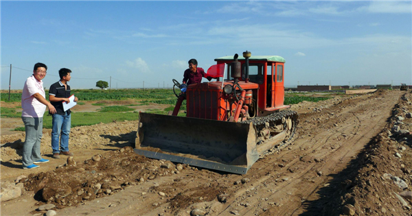 government officials from the local transportation department help guide farmers to pave the road with a tractor shovel 