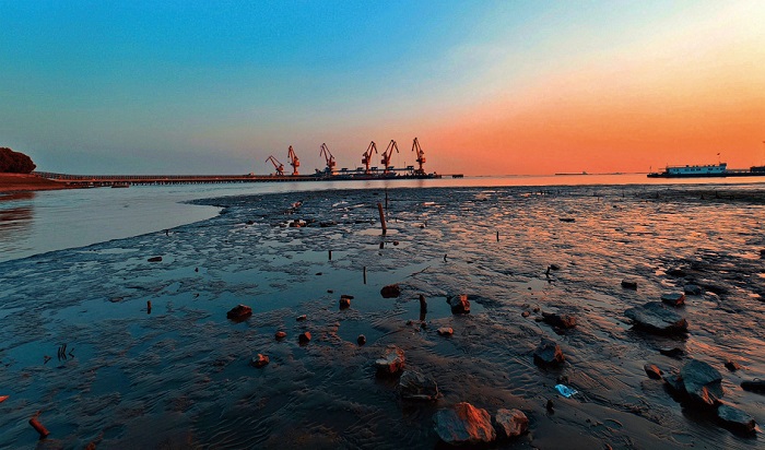 4 7月13日，南通市区裤子港，夕阳西沉，江边的红色钢铁吊塔与岸上的嶙峋礁石浸润在琥珀色光晕中，与天际的彩霞浑然一体。谢静玲 摄.jpg